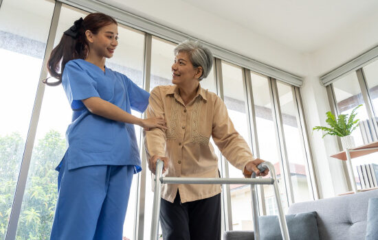 Asian Young physical therapist female help aged female patient walk with walker at home, aftercare and physiotherapy concept